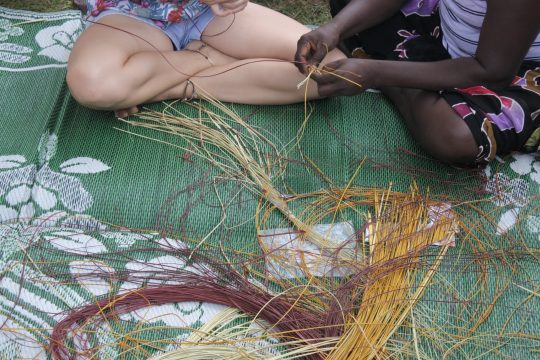 Indigenous Australians aboriginal woman teaching a tourist Aboriginal basket weaving technique.